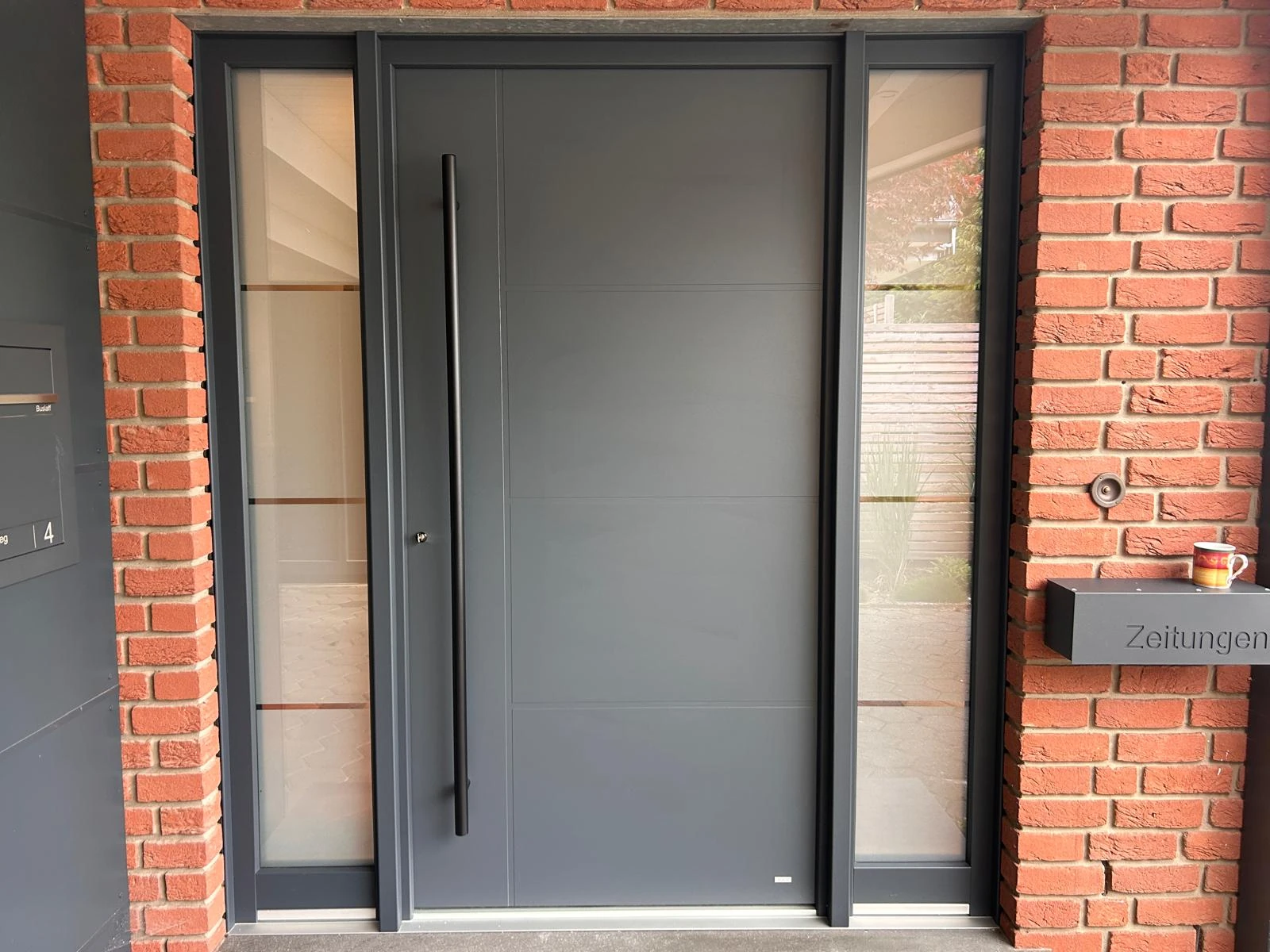 Haustür aus Aluminium mit zwei Seitenteilen in einer Klinkerfassade